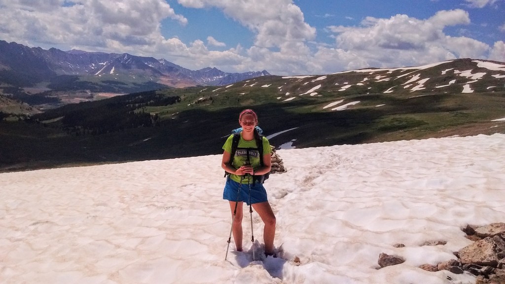 A hiker with trekking poles standing in ankle-deep snow