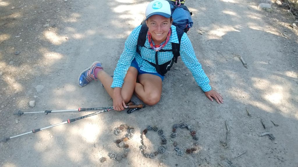 A hiker sitting on the ground next pinecones arranged to form the number "300"