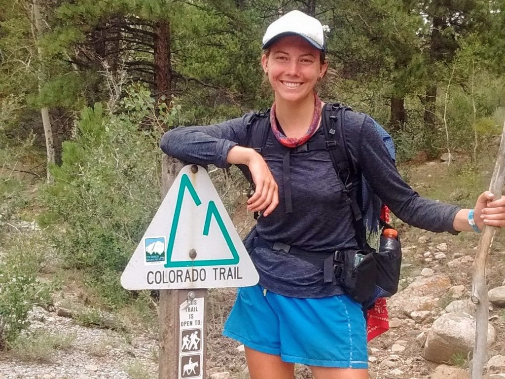 A hiker rests her elbow on a Colorado Trail sign