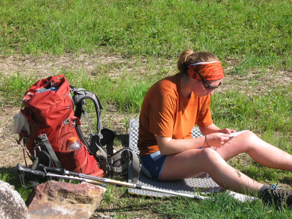 Hiker sitting looking at paper next to a backpack
