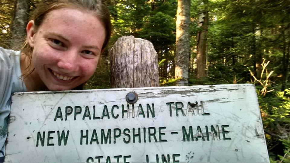 hiker with the New Hampshire-Maine state line sign on the Appalachian Trail